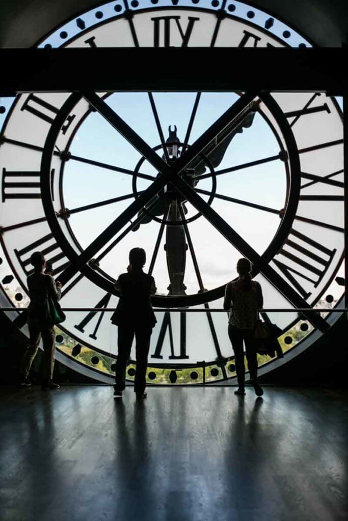 Three people looking at the backside of a working clock-shaped window.