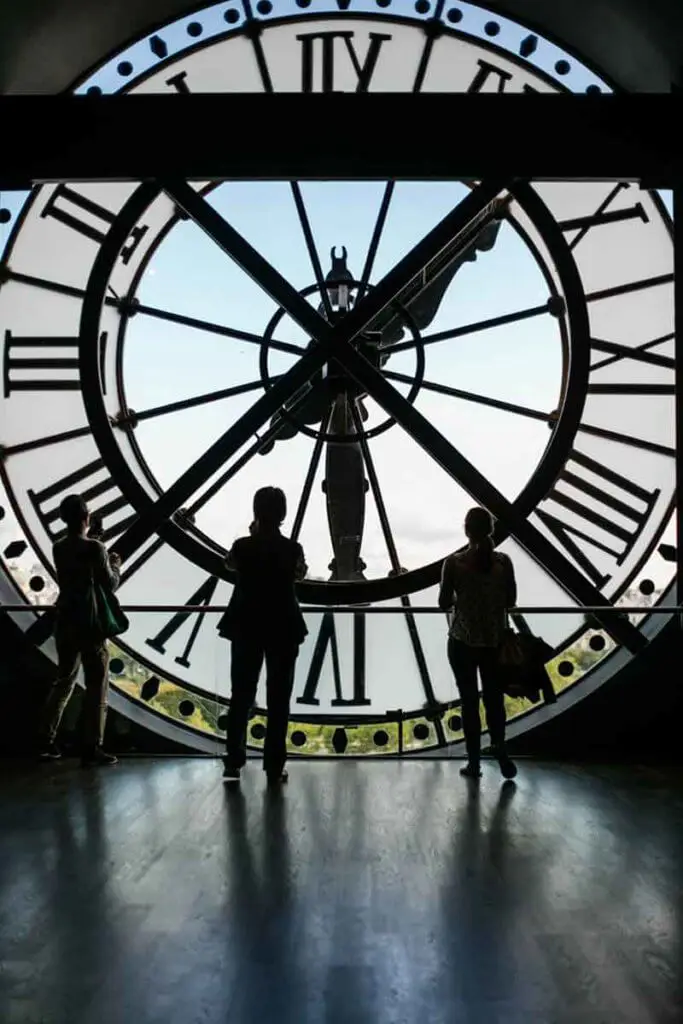 Three people looking at the backside of a working clock-shaped window.