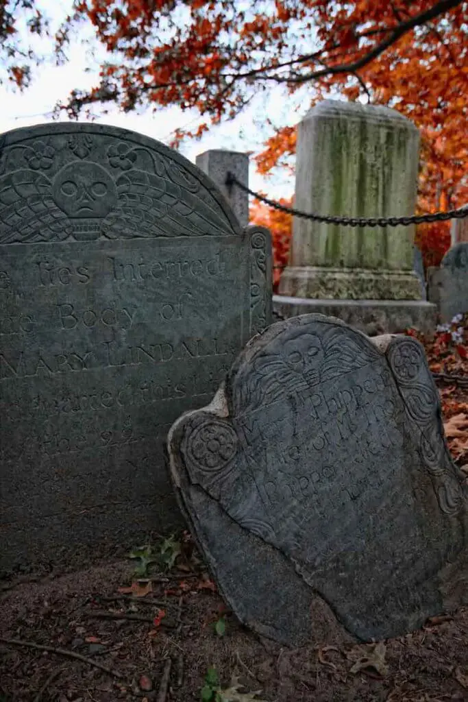 Closeup of 2 old gravestones amidst red fallen leaves.