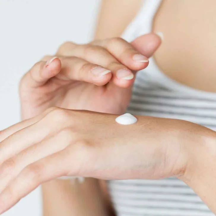 Closeup of a woman about to rub a drop of sunscreen on her hand.