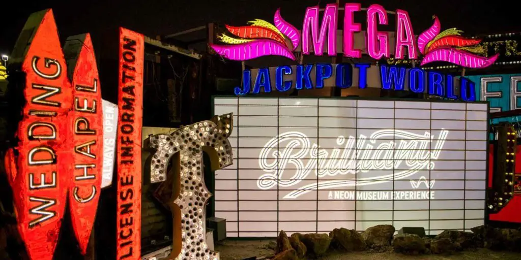 Closeup of old neon light signs stacked artfully. A sign says "Brilliant! A Neon Museum Experience."