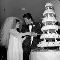 Historical photography of Elvis and Priscilla Presley on their wedding day, cutting a 6-tier weddingcake.