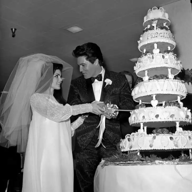 Historical photography of Elvis and Priscilla Presley on their wedding day, cutting a 6-tier weddingcake.
