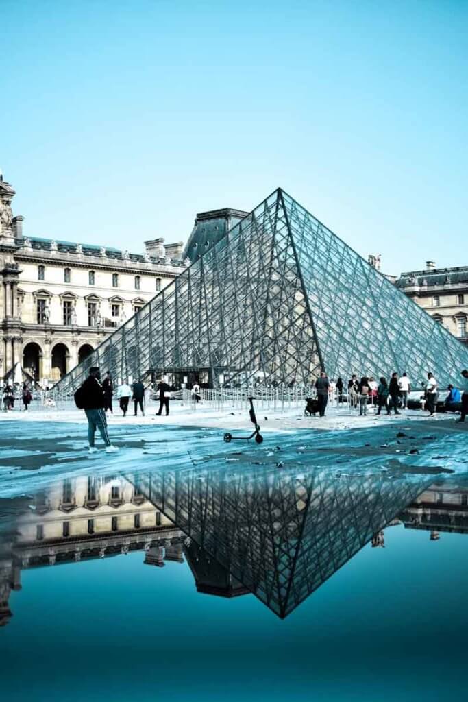 Closeup view of the iconic glass pyramid at the Louvre, reflecting in a puddle of water.