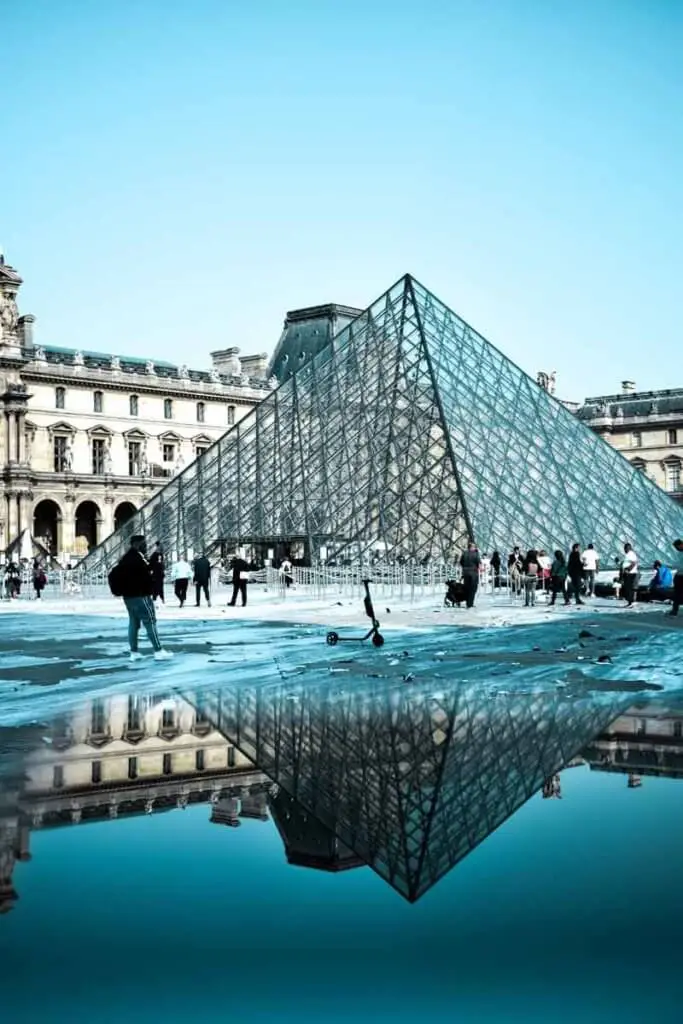 Closeup view of the iconic glass pyramid at the Louvre, reflecting in a puddle of water.