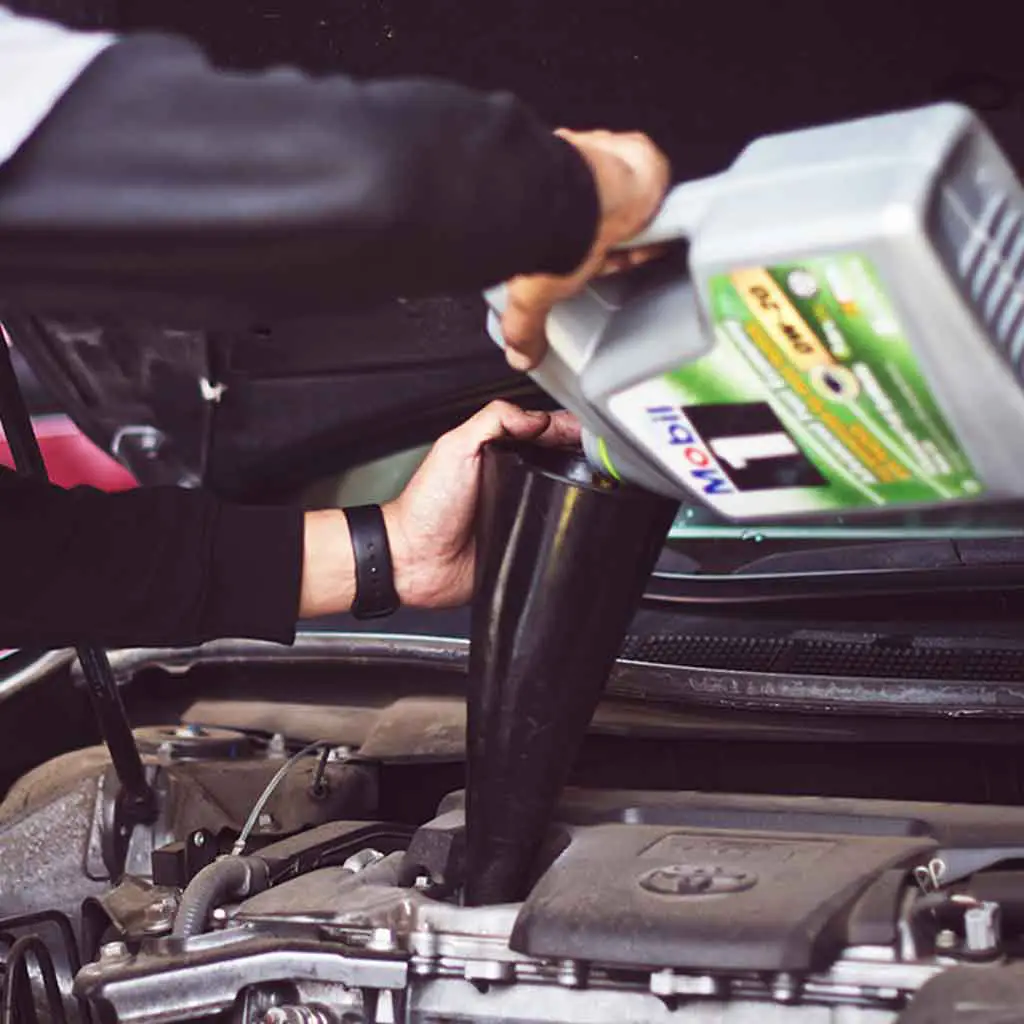 Closeup of a person pouring motor oil into a funnel over a car engine.