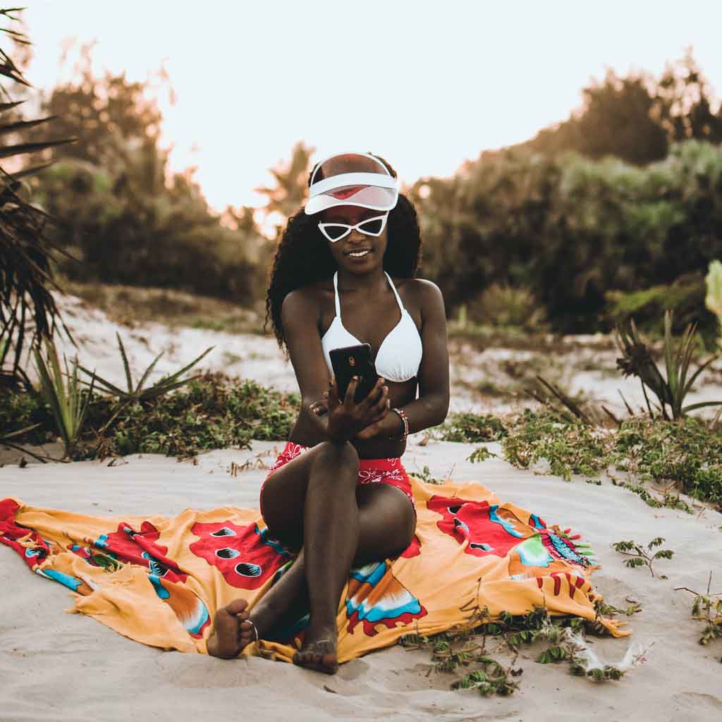 Photograph of a woman in a bikini looking at her phone while lounging on a beach.