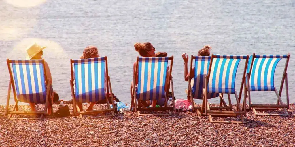 Photograph of striped beach chairs with a few women sitting on them set on sand overlooking the ocean.