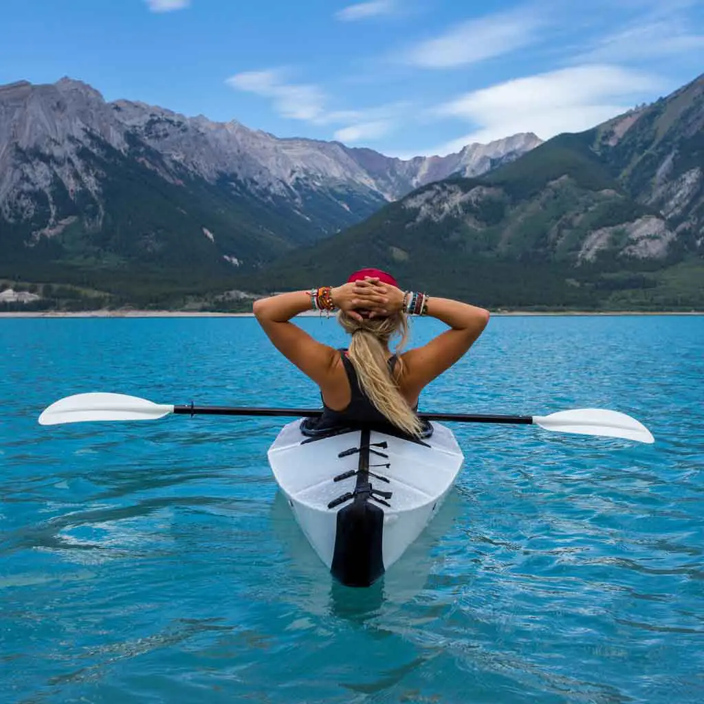 Photograph of a woman in a white kayak on turquoise waters resting with her hands on the back of her head looking out to mountains in the distance.