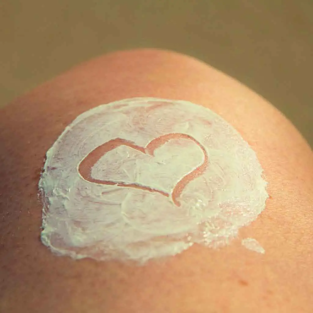 Close up light skin with sunscreen partially rubbed in with a heart traced in the middle.
