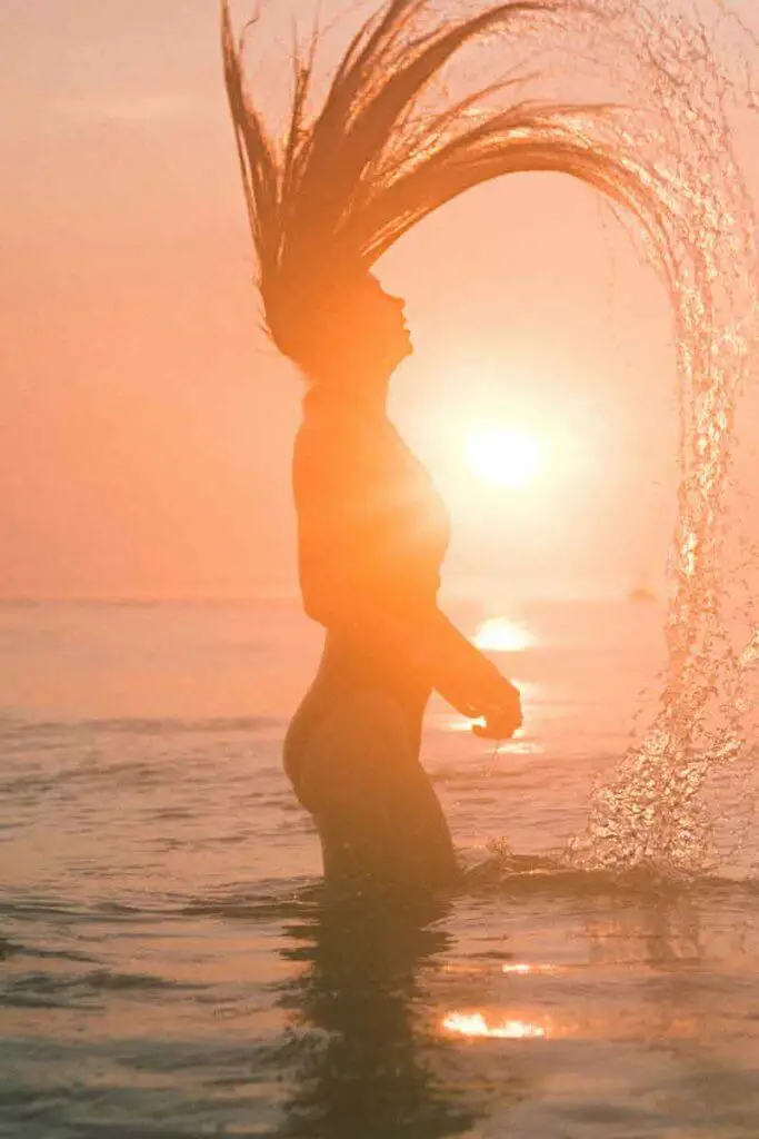 Silhouette of a woman in an ocean flipping her hair back with a trail of water following.