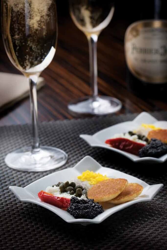 Closeup of 2 plates of caviar and accompaniments and 2 glasses of champagne.