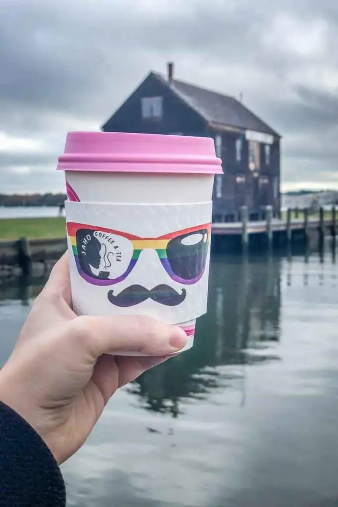 Photo of a person holding a cup of coffee near a waterfront location.