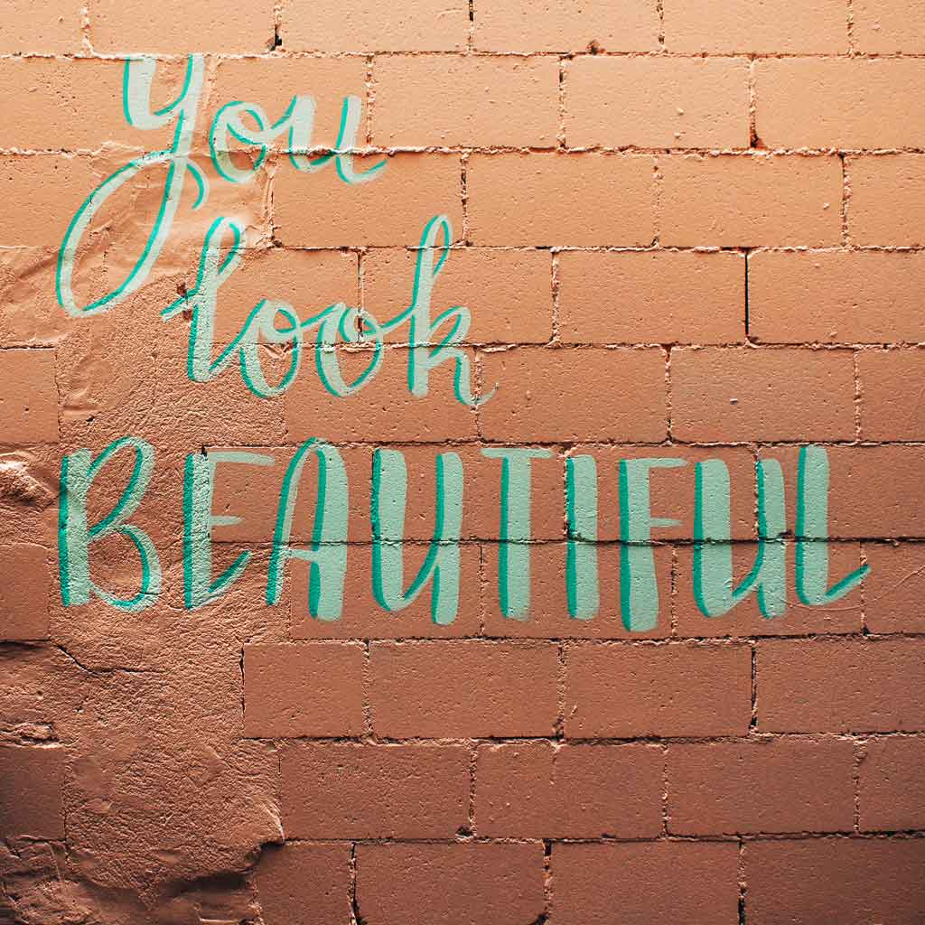 Photo of a peachy pink brick wall with the phrase "You look beautiful," painted on it.