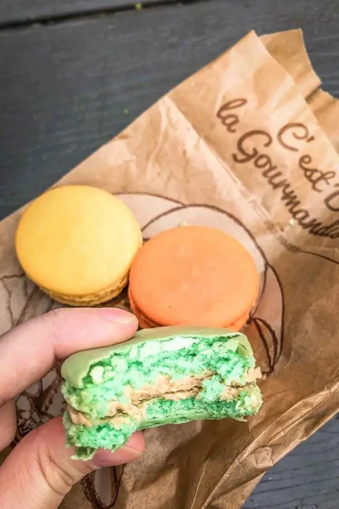 Closeup photo of a person holding a partially eaten macaron with several arranged on a table below.