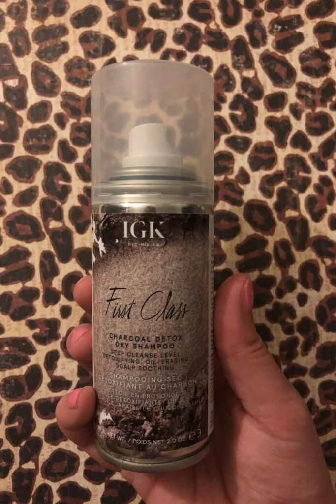 Closeup photo of a hand holding a can of IGK First Class Charcoal Detox dry shampoo.