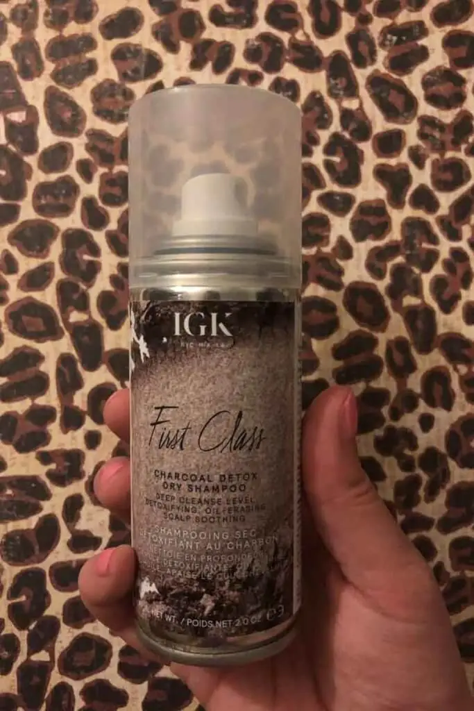 Closeup photo of a hand holding a can of IGK First Class Charcoal Detox dry shampoo.
