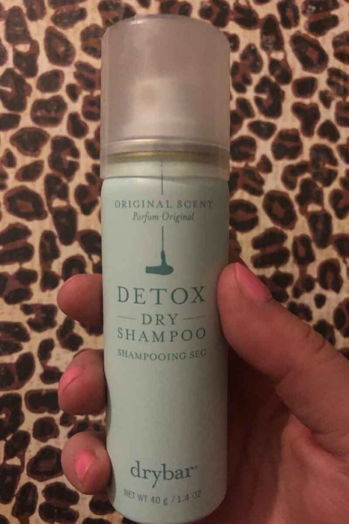 Photo of a hand holding a small can of drybar Detox dry shampoo.