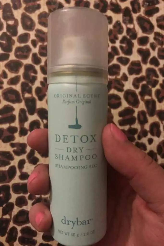 Photo of a hand holding a small can of drybar Detox dry shampoo.