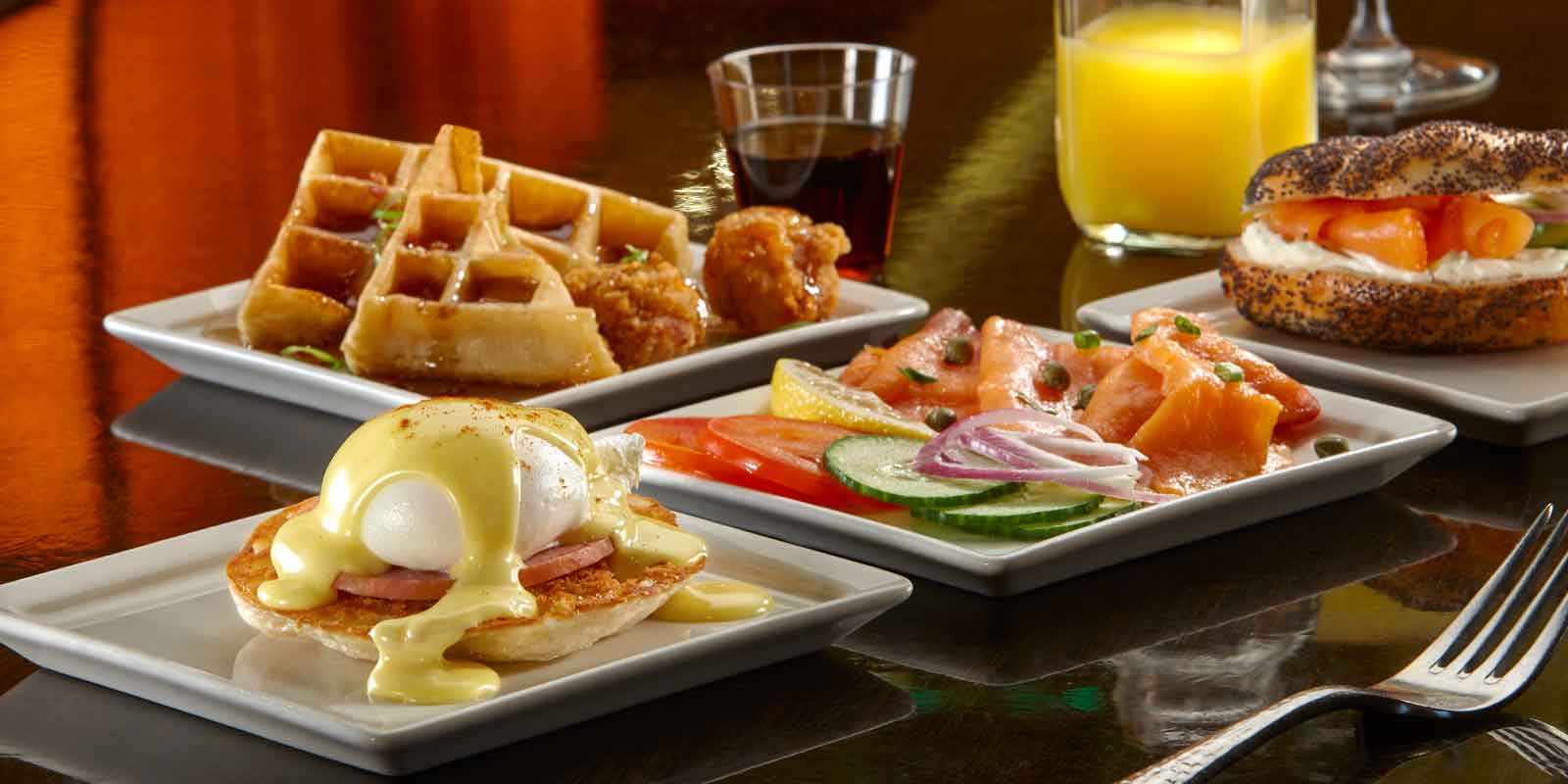 Photo of a spread of breakfast foods, like eggs benedict, waffles, and a bagel with lox.