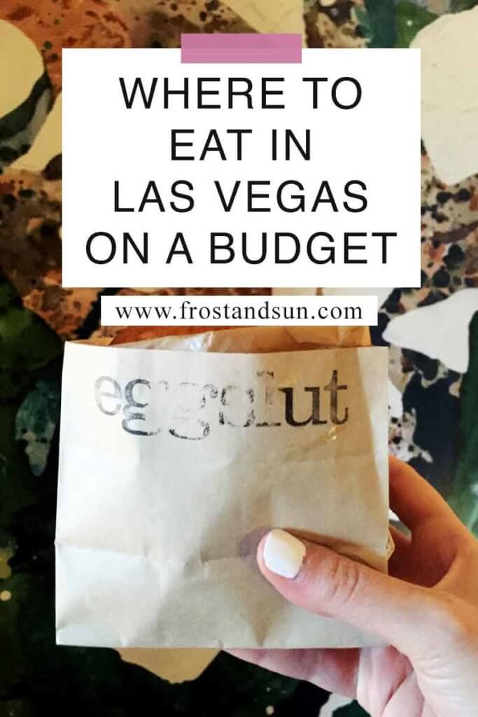 Close up of a breakfast sandwich in a brown wrapper held up in front of a wallpapered wall. Overlying text reads "Where to Eat in Las Vegas on a Budget."