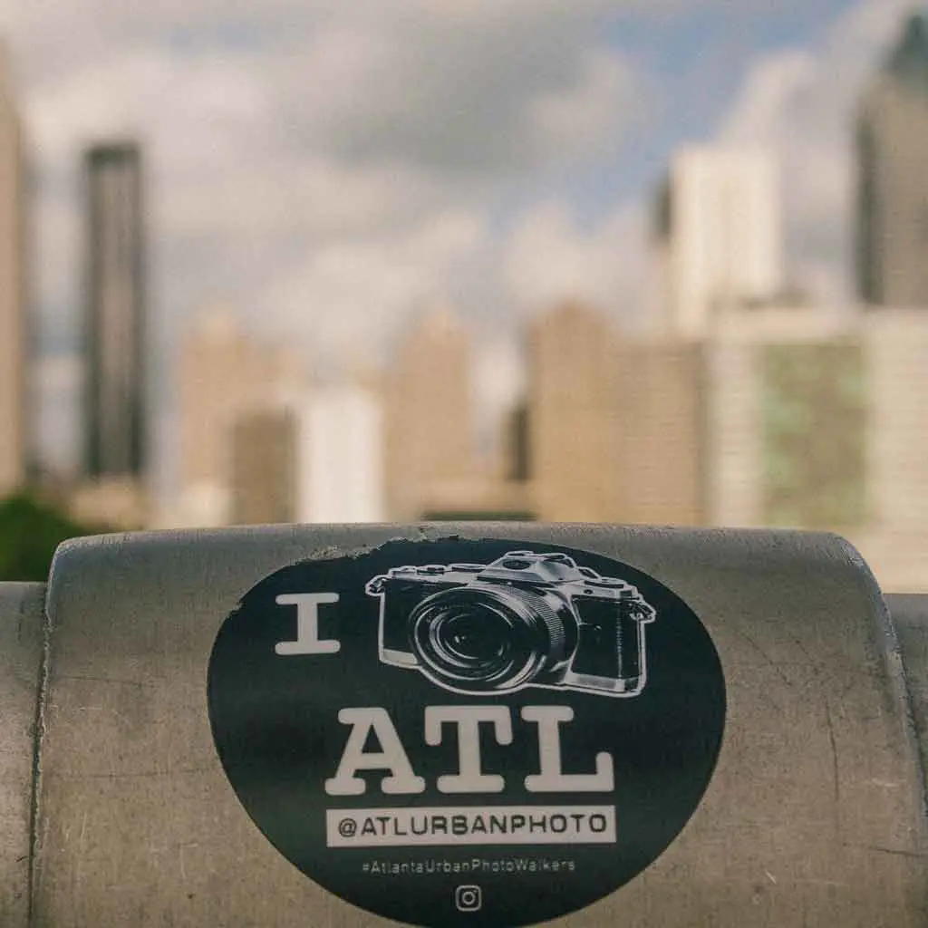 Close up of a sticker on a railing that reads "I [picture of camera] ATL."