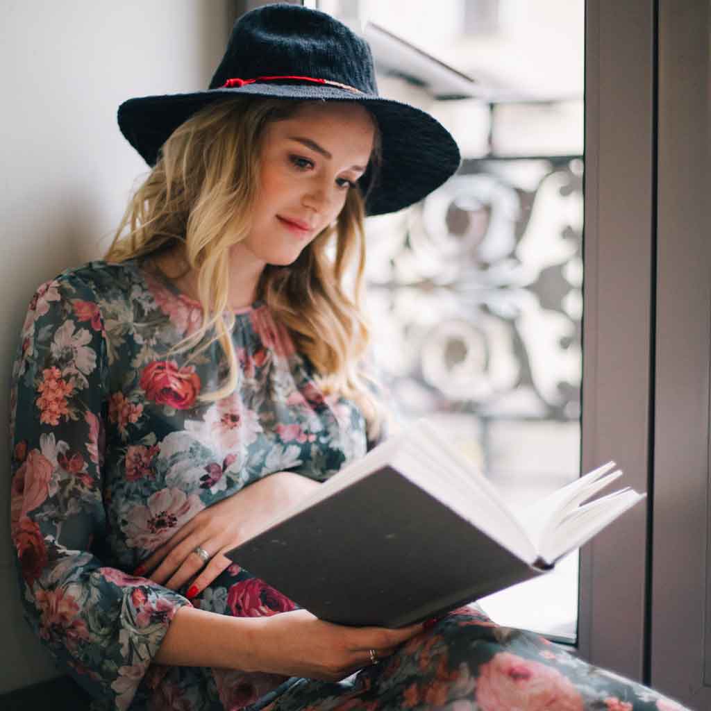 Photo of a slightly pregnant woman leaning against a wall while reading a book.