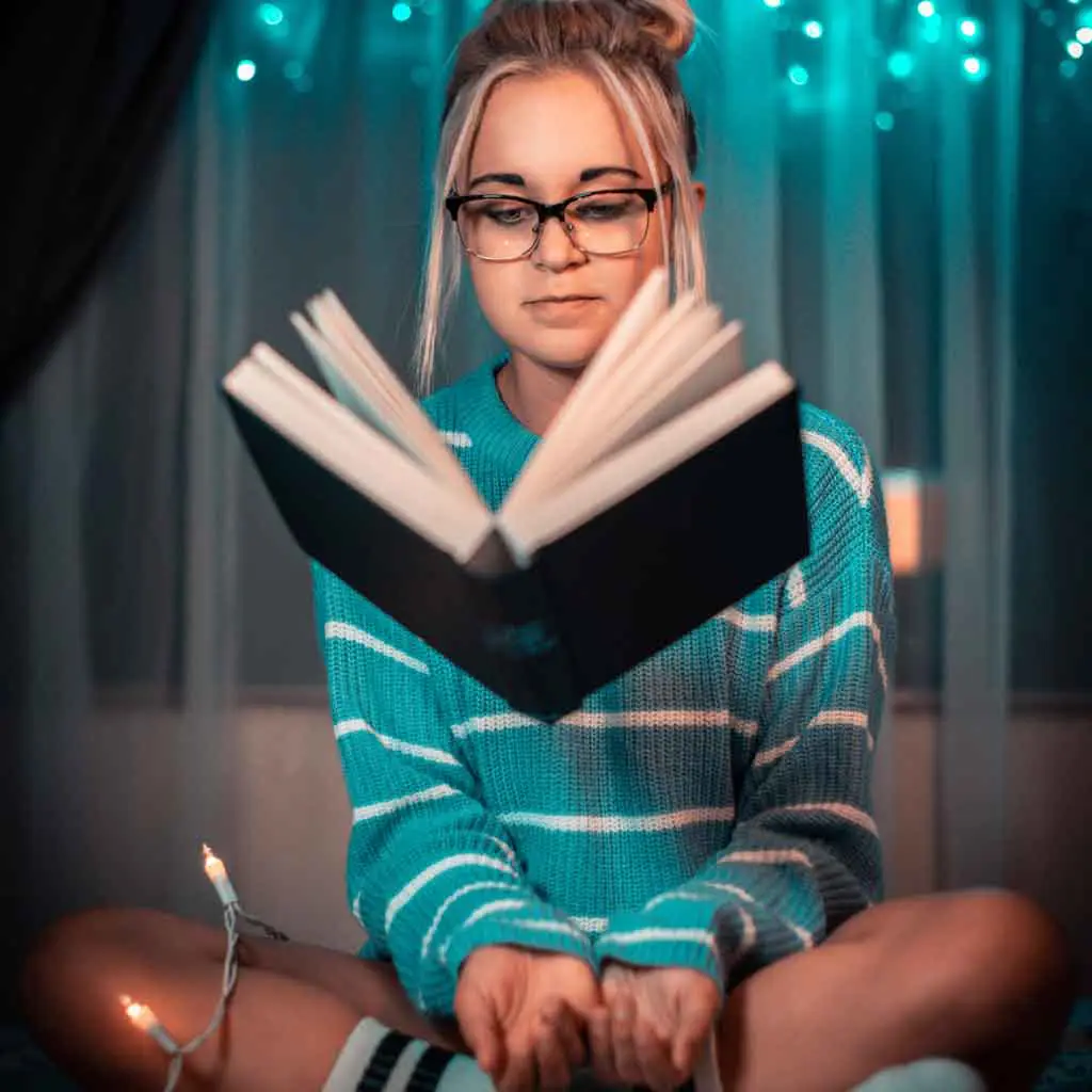 Photo of a young woman sitting with crossed legs with a book levitating in front of her.