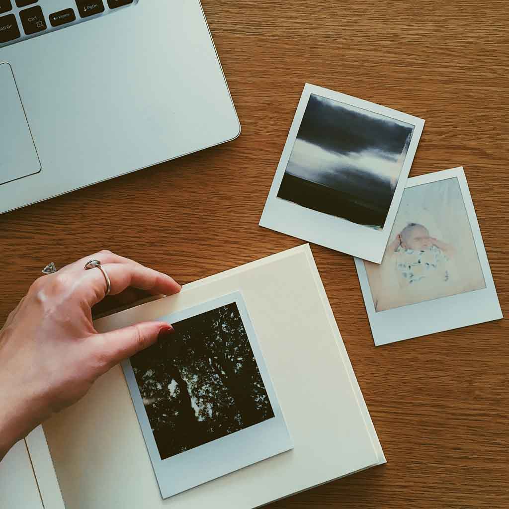Closeup of a woman placing a Polaroid photo on a blank scrapbook album.