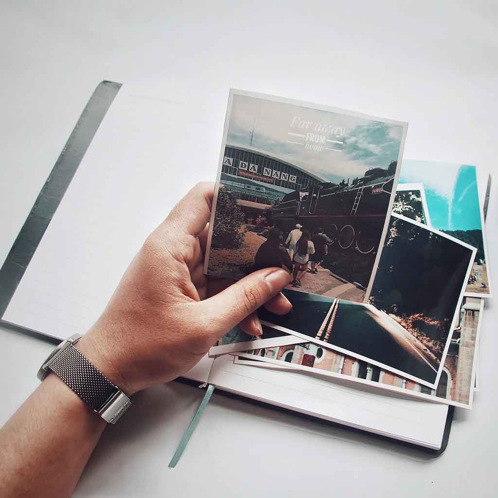 Picture of a person holding a photo above a notebook and stack of more photos.