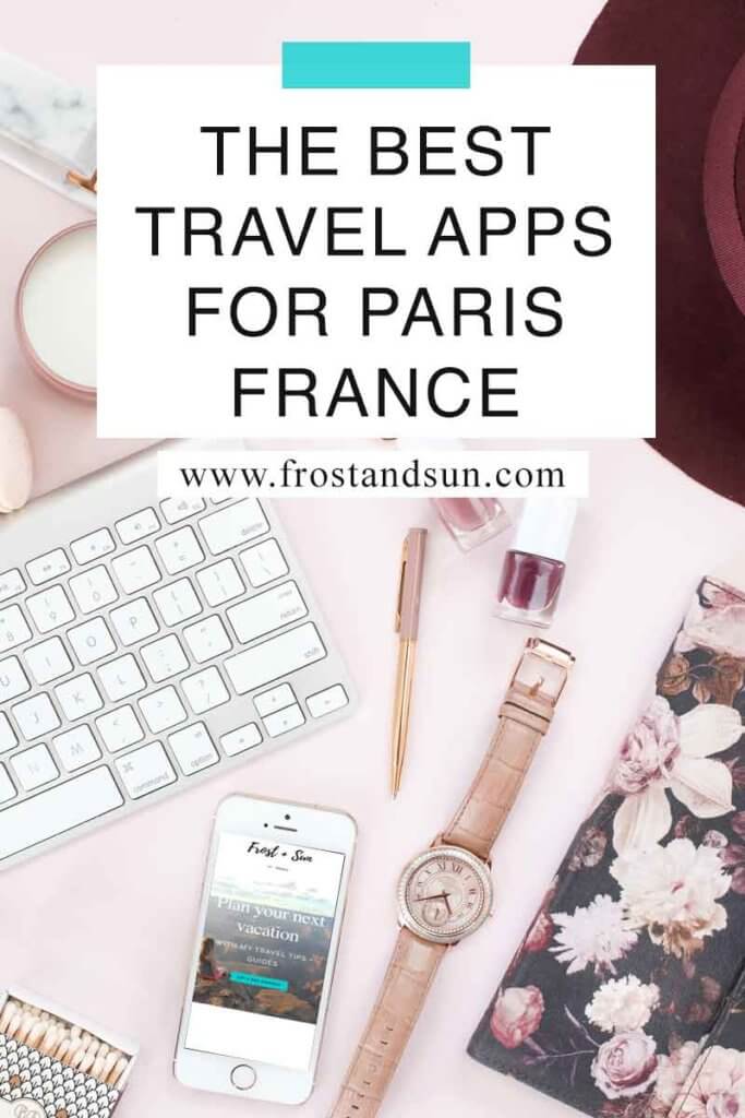 Flat lay photo of a pink surface with a maroon wool hat, nail polish, a white and silver keyboard, a watch with a tan band, and an iphone showing the Frost + Sun travel blog home page. Overlying text reads "The Best Travel Apps for Paris, France."