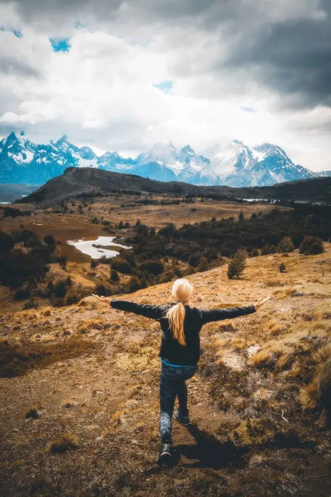 Landscape view of a woman with her arms outstretched while overlooking the landscape and mountains in Patagonia.