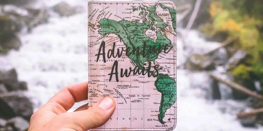 Closeup of a person holding a passport cover with an image of a map and the words "Adventure Awaits."