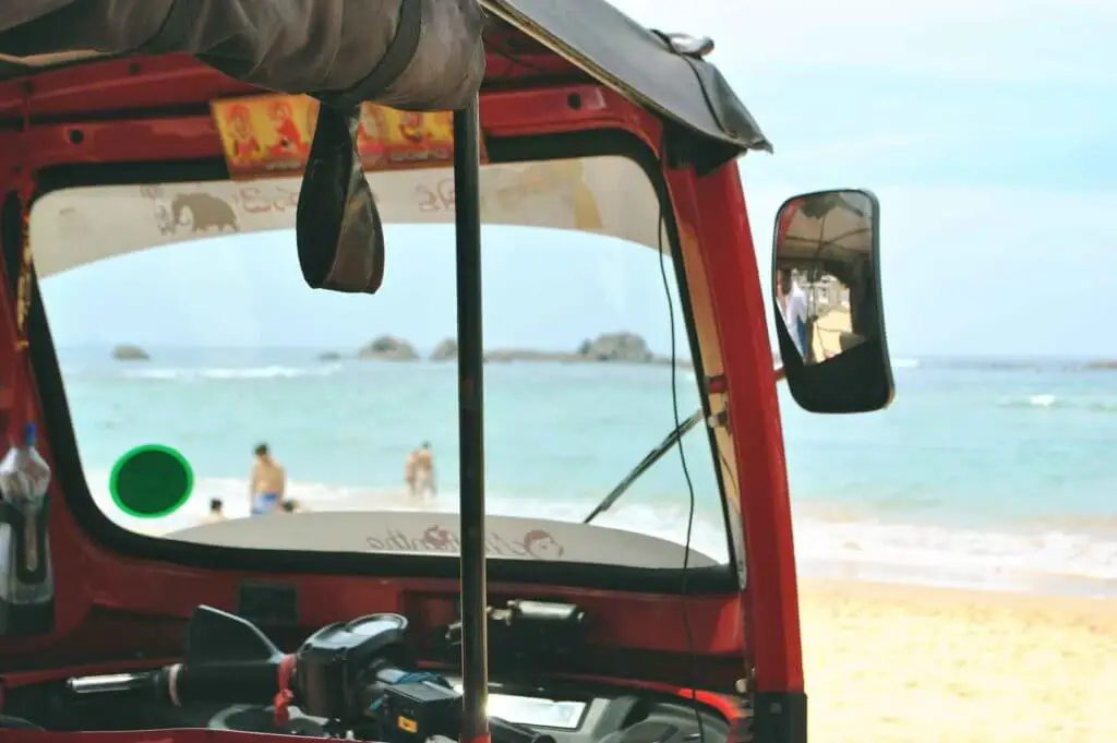 Closeup of a tuk tuk vehicle parked while looking out to a beach and ocean.