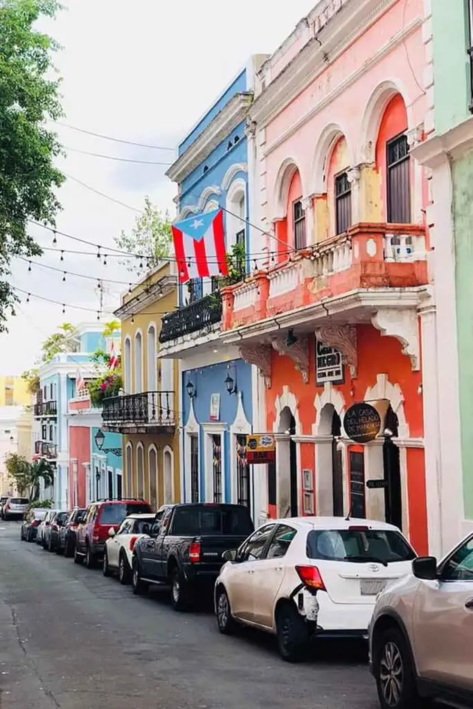 Photo of a street in Puerto Rico with colorful buildings on one side and a line of cars parked on the side of the street.