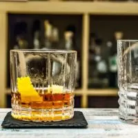 Closeup of a classic Sazerac cocktail on top of a black stone coaster on a bar.