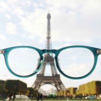 Photo of the Eiffel Tower through a pair of turquoise glasses held in front of the camera.