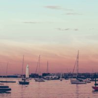 Photo of the Boston skyline during sunset with boats in the water.