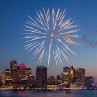 Photo of the Boston skyline from across the Charles River. A massive firework is exploding in the sky.