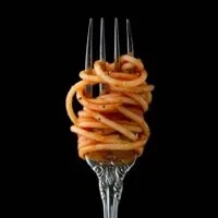 Closeup of a fork with spaghetti twirled around it, held up against a black background.