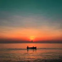 Photo of a gorgeous orange and teal sunset with a silhouette of a small boat with 2 people in it.