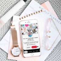 Flat lay photo with gray, pink, and white objects artfully arranged. In the middle is an iPhone open to a Pinterest profile page.