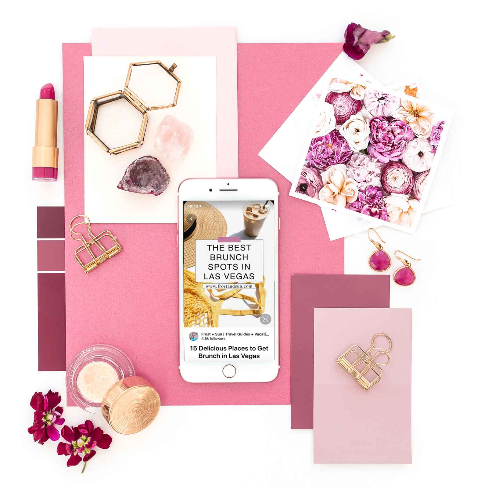 Flat lay of pink and gold objects, such as lipstick, papers, flowers, and makeup, artfully arranged. In the middle is a white iPhone open to a pin on Pinterest with extra data like profile photo, profile name, and blog post title.