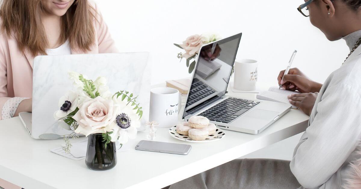 Closeup photo of 2 women working at a desk with laptops open.