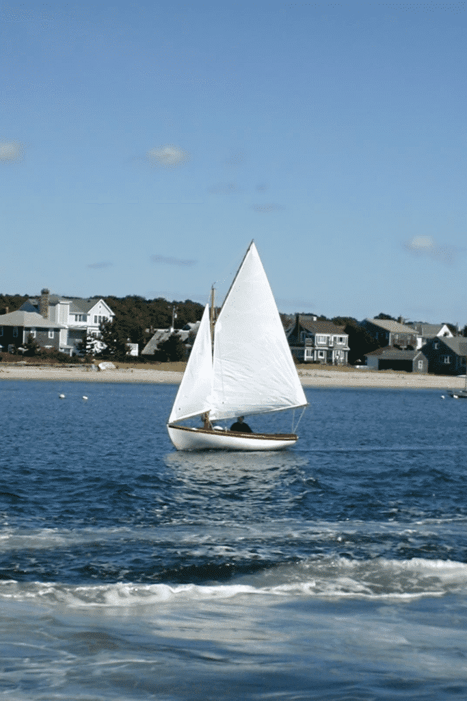 Photo of a small sail boat on the ocean with the shore not far away.