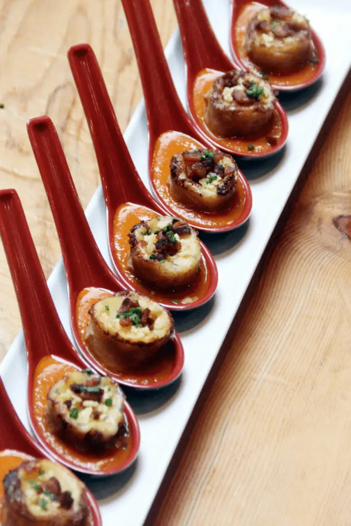 Closeup of a row of tasting spoons with grilled cheese dumplings atop tomato soup.