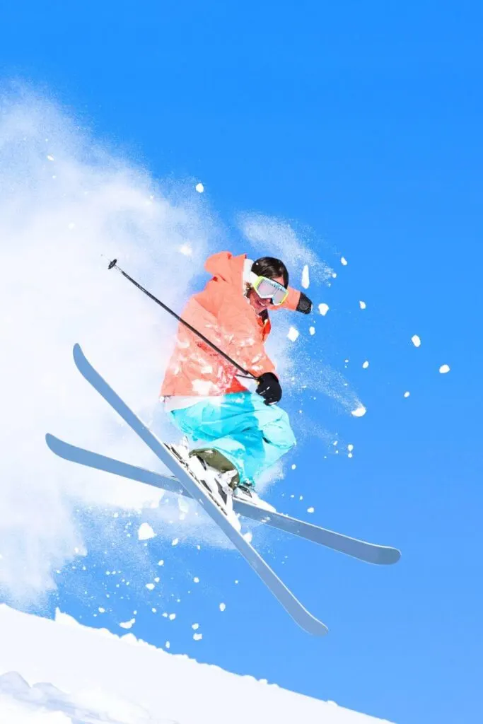 Photo of a person in colorful snow gear on skis mid-air off a ski jump.