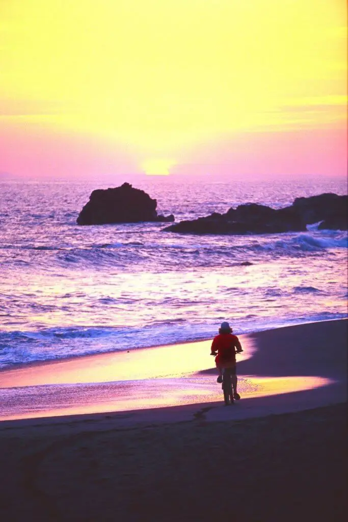 Photo of a person riding a bike on a beach during sunset.