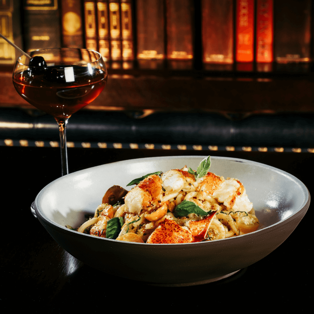 Closeup of a bowl of lobster fra diavolo and a delicious cocktail.