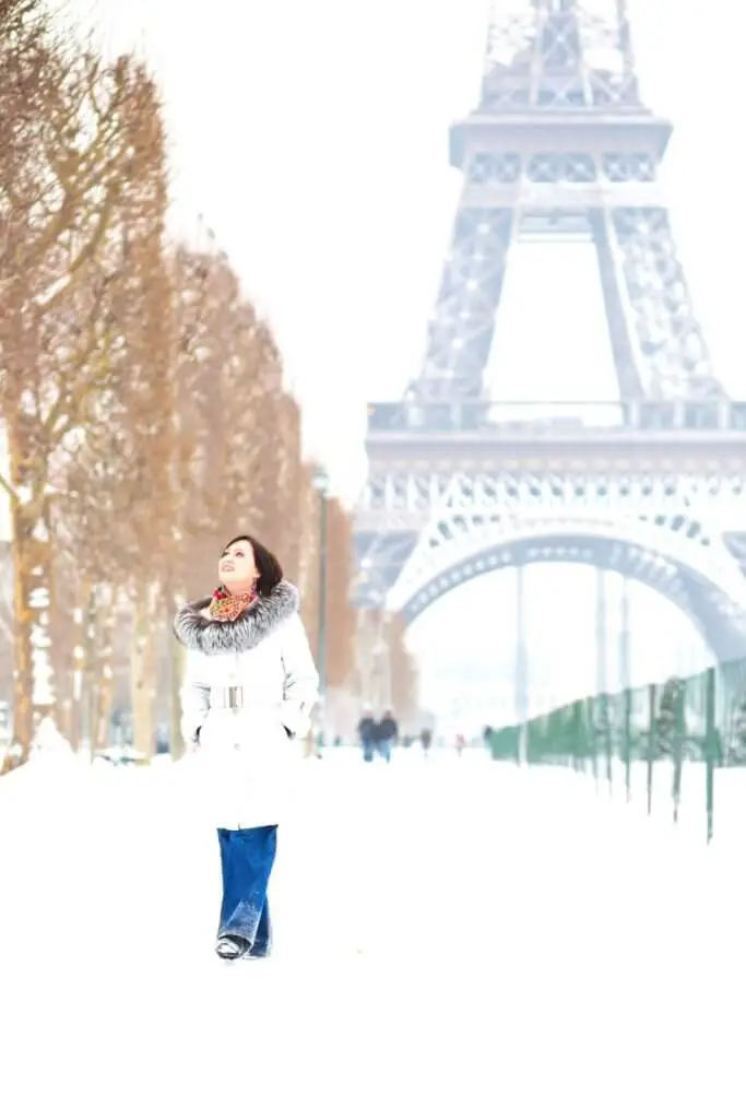 Photo of a woman walking through the snow with the Eiffel Tower in the background.